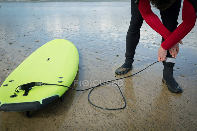 Surfer attaching surfboard string to his leg on beach — Stock Photo