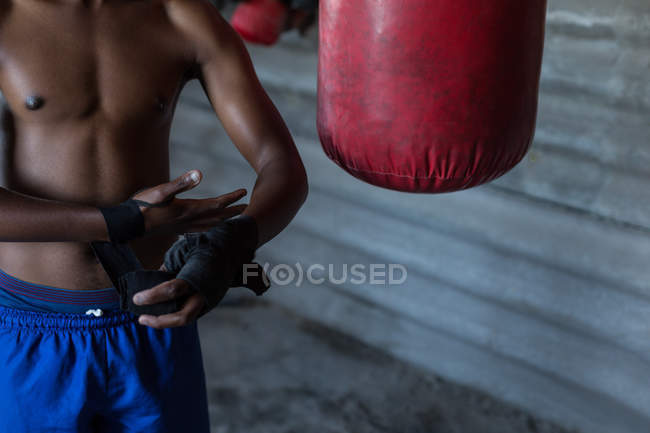Средняя секция мужского боксера, связывающего ручную пленку на руках в фитнес-студии — стоковое фото