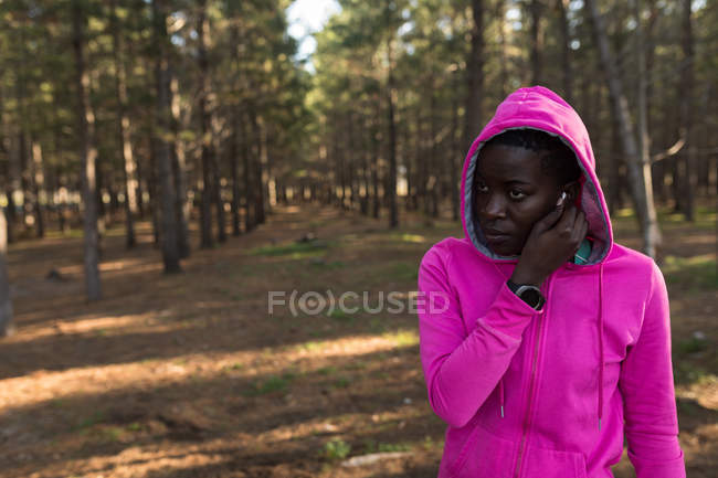 Female athlete in hooded jacket listening to music in the forest — Stock Photo