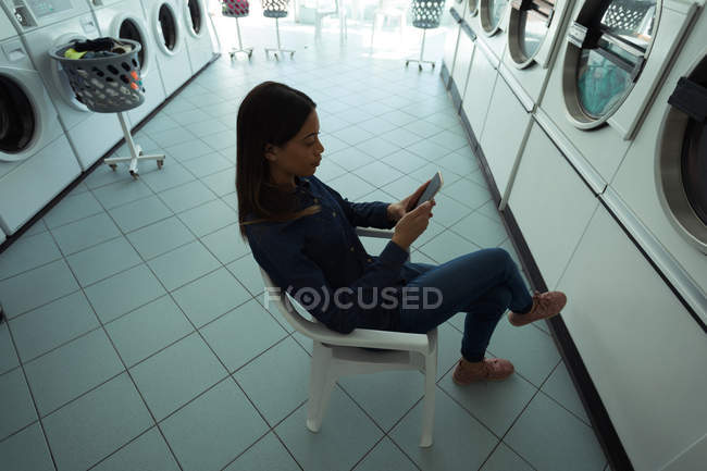 Jovem mulher usando seu telefone enquanto espera na lavanderia — Fotografia de Stock