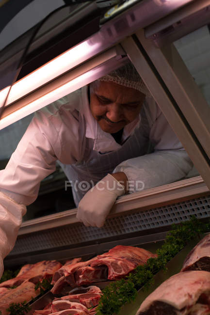 Macellaio che rimuove la carne dall'esposizione in macelleria — Foto stock