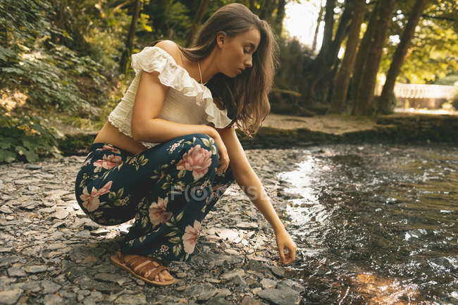 Nahaufnahme einer Frau, die in der Nähe der Flussküste im grünen Wald kauert — Stockfoto
