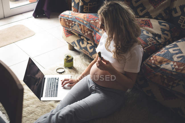 Mujer embarazada usando el ordenador portátil en la sala de estar en casa - foto de stock