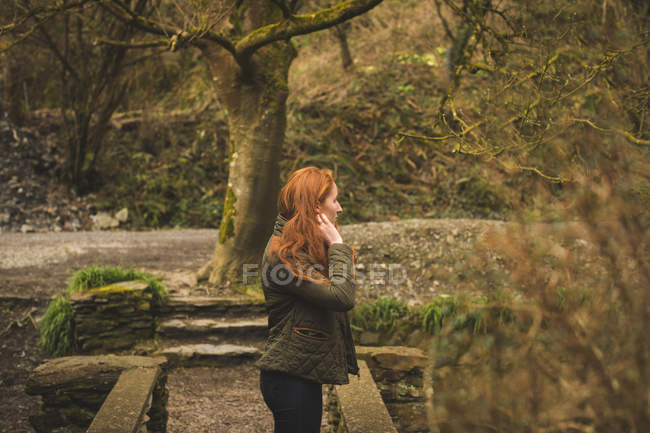 Hermosa senderista de pelo rojo mirando alrededor en el bosque - foto de stock