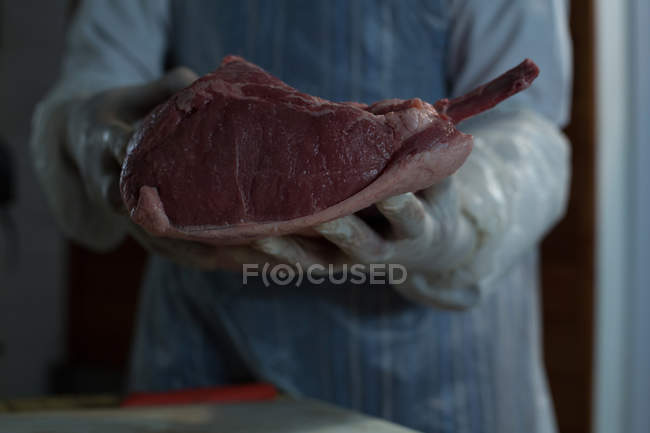Средняя часть мясника держит мясо в руках в мясной лавке — стоковое фото