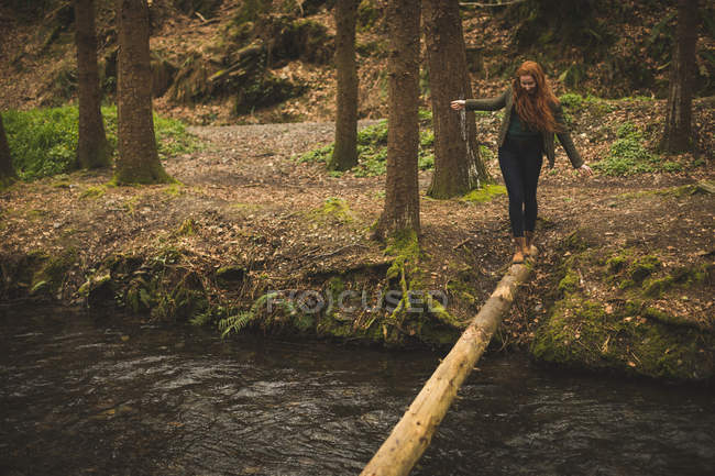 Caminhante feminina caminhando no tronco da árvore caída através do rio na floresta — Fotografia de Stock