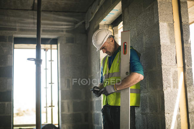 Engineer with level gauge using his phone at the construction site — Stock Photo