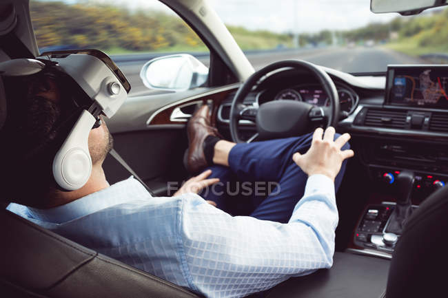 Hombre de negocios con auriculares de realidad virtual en un coche moderno - foto de stock