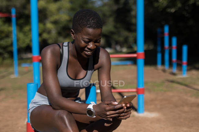 Atleta feminina sorrindo usando seu telefone perto das barras — Fotografia de Stock