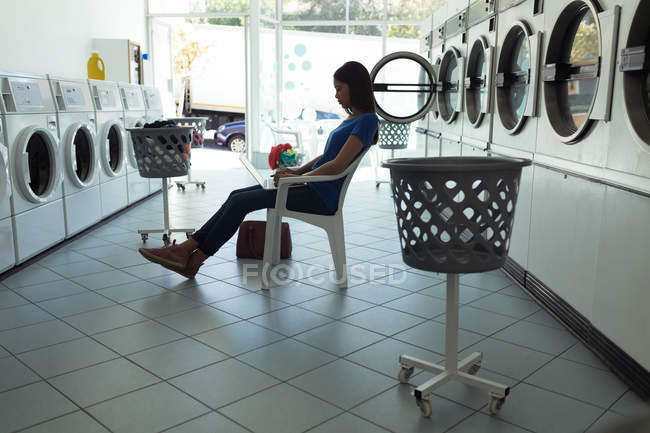Концентрована жінка використовує ноутбук на пральні — стокове фото