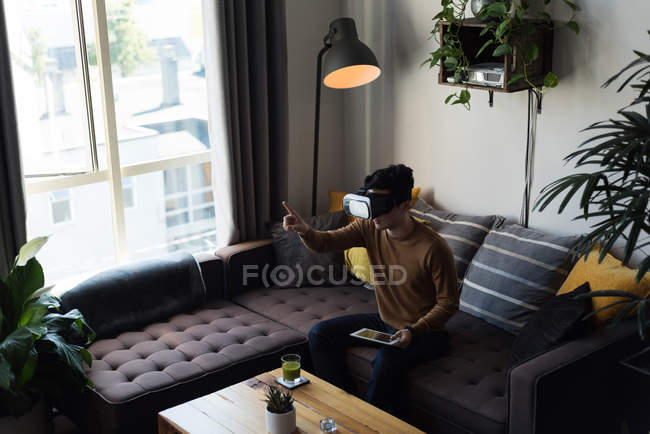 Человек в гарнитуре виртуальной реальности с помощью цифрового планшета в гостиной дома — стоковое фото