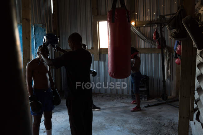 Treinador ajudando boxeador masculino a usar chapelaria no estúdio de fitness — Fotografia de Stock