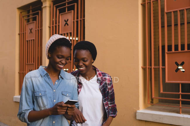 Jumeaux frères et sœurs utilisant un téléphone portable tout en marchant sur un trottoir dans la ville — Photo de stock
