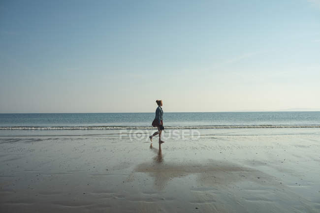 Femme marchant sur la plage par une journée ensoleillée — Photo de stock