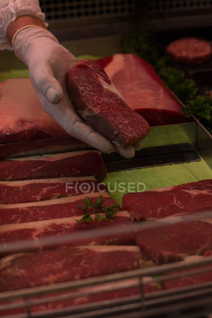 Açougueiro retirando carne da exposição no açougue — Fotografia de Stock