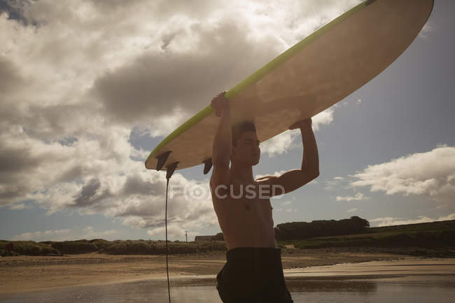 Surfista carregando a prancha na cabeça em um dia ensolarado — Fotografia de Stock