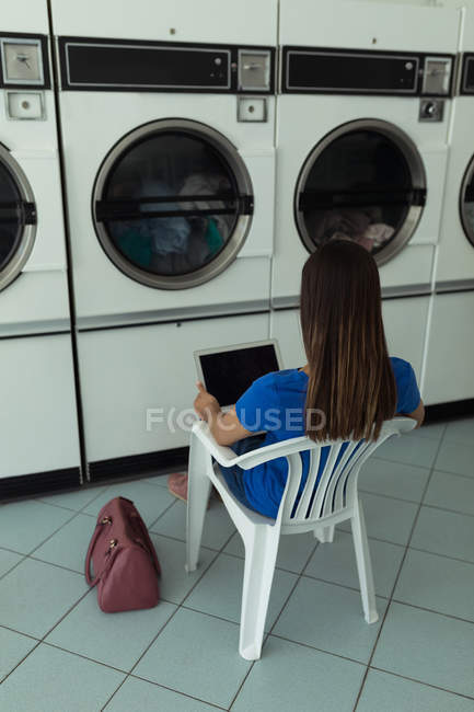 Rear view of woman using laptop at laundromat — Stock Photo
