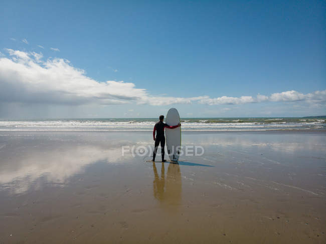 Rückansicht eines Surfers mit Surfbrett, der vom Strand aus auf das Meer blickt — Stockfoto