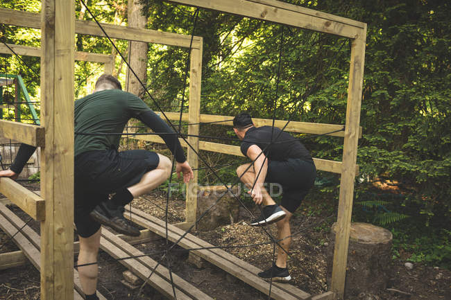 Двое мужчин тренируются на полосе препятствий в учебном лагере — стоковое фото