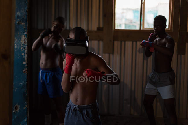 Boxeador masculino usando auriculares de realidad virtual mientras practica boxeo en un gimnasio - foto de stock