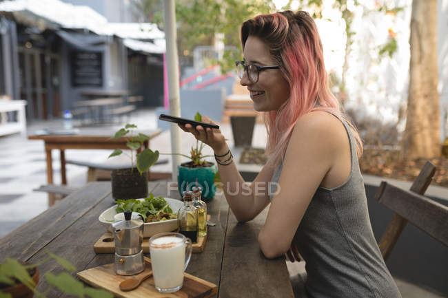 Jeune femme photographiant de la nourriture servie sur la table dans un café — Photo de stock