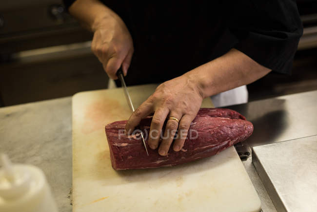 Seção intermediária do chef masculino cortando carne na cozinha — Fotografia de Stock