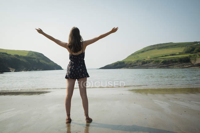 Rückansicht einer Frau, die mit ausgebreiteten Händen am Strand steht — Stockfoto