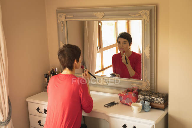 Mulher aplicando maquiagem na frente do espelho no quarto em casa — Fotografia de Stock