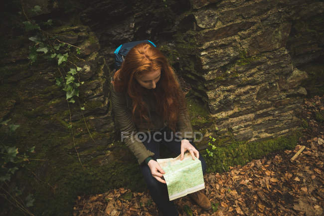 Рыжеволосая женщина-туристка с рюкзаком читает карту в лесу — стоковое фото