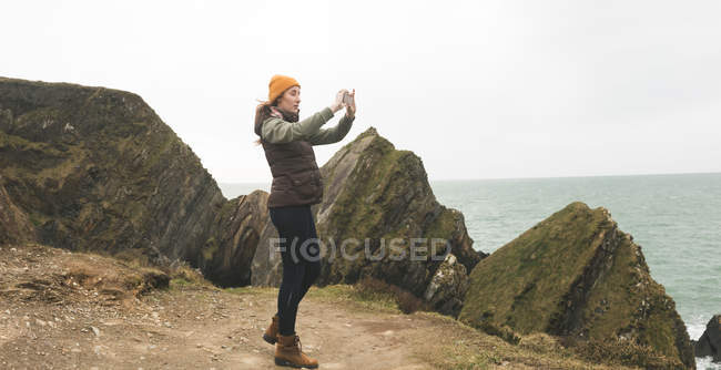 Вид сбоку женщины-туристки, фотографирующей море — стоковое фото