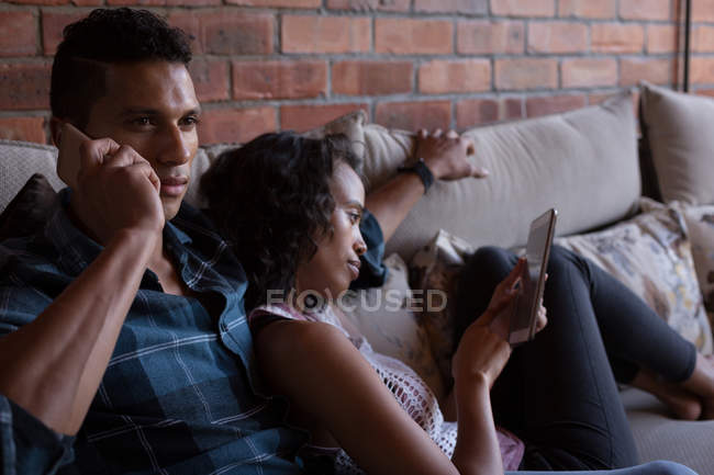 Casal usando tablet digital e conversando no celular em casa — Fotografia de Stock
