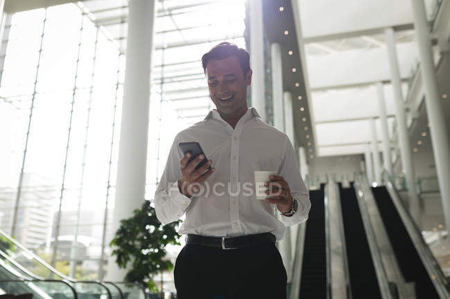 Lächelnder Geschäftsmann checkt im Büro sein Telefon — Stockfoto