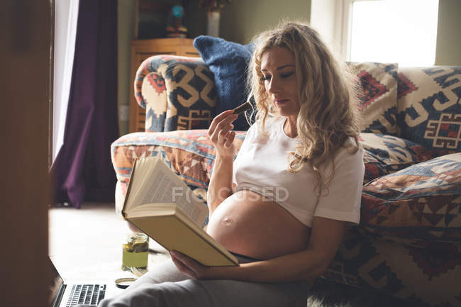 Вагітна жінка читає книгу у вітальні вдома — стокове фото