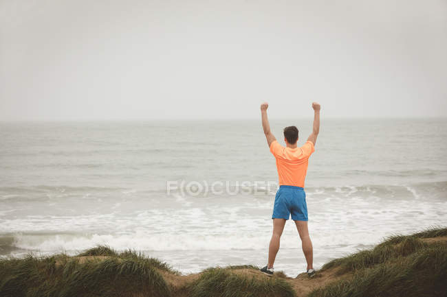 Visão traseira do homem de pé com a mão levantada na praia — Fotografia de Stock