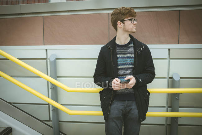 Schöner junger Mann lehnt mit Handy am Geländer — Stockfoto