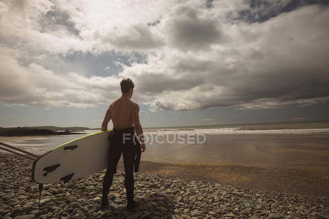 Surfer with surfboard looking at the sea from beach on a sunny day — Stock Photo