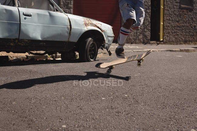 Bassa sezione di uomo che salta sullo skateboard in strada alla luce del sole — Foto stock