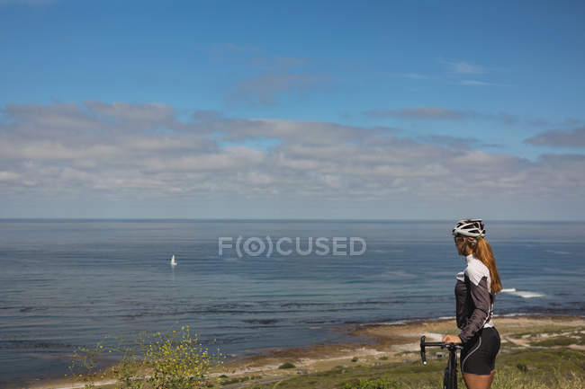 Feminino motociclista com mountain bike olhando para o mar em um dia ensolarado — Fotografia de Stock