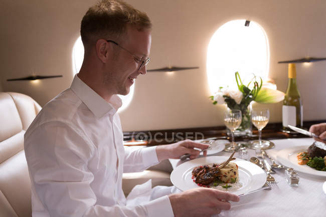 Medio hombre de negocios adulto comiendo mientras viaja en jet privado - foto de stock