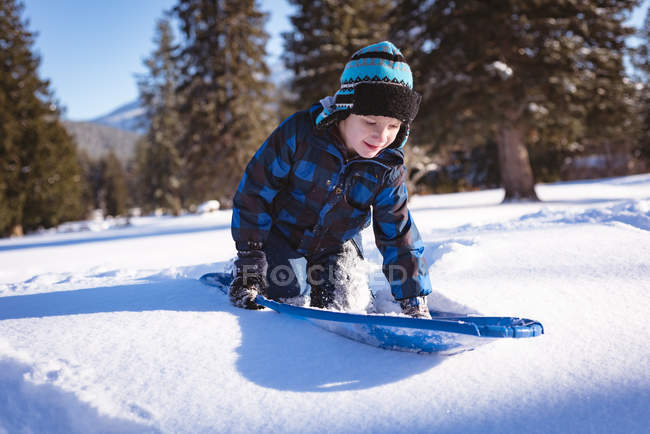 Cute boy playing with sled in snow during winter — Stock Photo