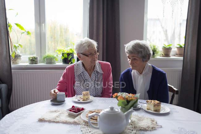 Старші друзі взаємодіють один з одним, снідаючи вдома — стокове фото