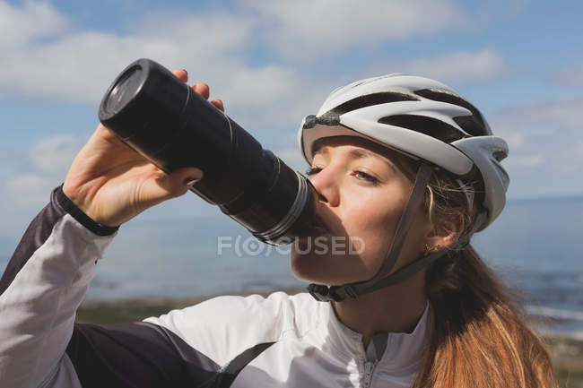 Close-up of female biker drinking water from bottle on a sunny day — Stock Photo