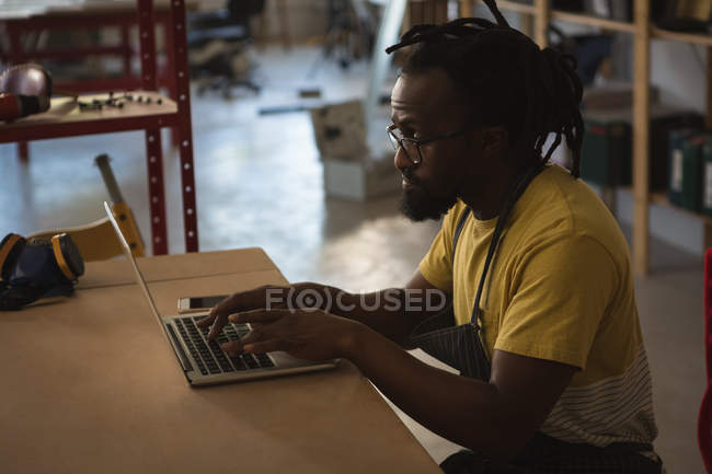 Плотник с ноутбуком за столом в мастерской — стоковое фото