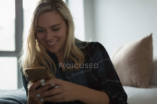 Mujer usando teléfono móvil en el dormitorio en casa - foto de stock