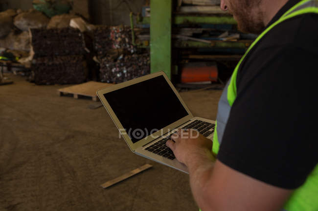 Sección media del trabajador que utiliza el ordenador portátil en el desguace - foto de stock