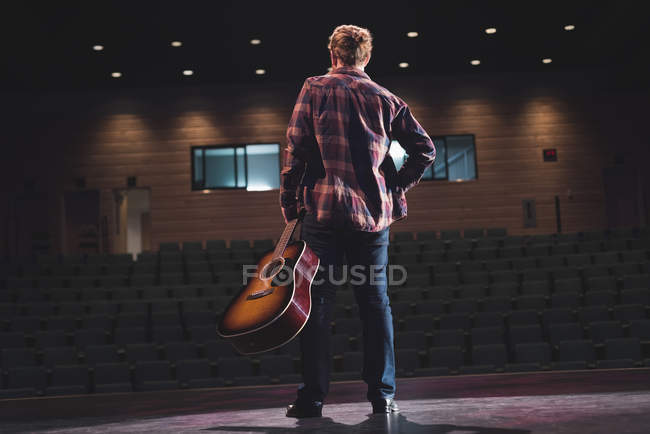 Man standing with guitar on stage at theatre. — Stock Photo