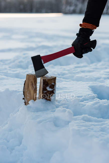 Male hand cutting wood log with axe in snow. — Stock Photo