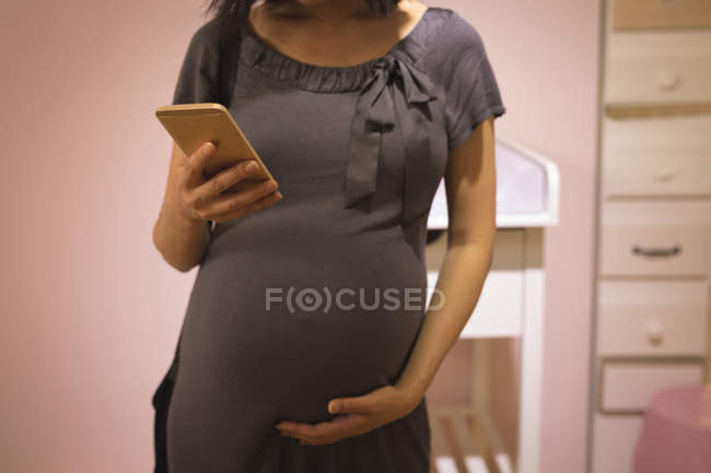 Беременная женщина прикасается к животу во время использования мобильного телефона в магазине — стоковое фото