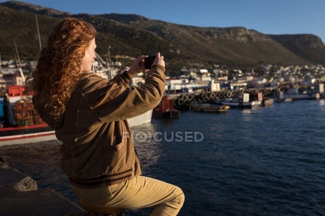 Woman taking photo of harbor with mobile phone in sunlight — Stock Photo