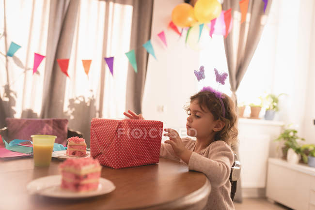 Kleines Mädchen betrachtet Geschenkbox im Wohnzimmer zu Hause. — Stockfoto